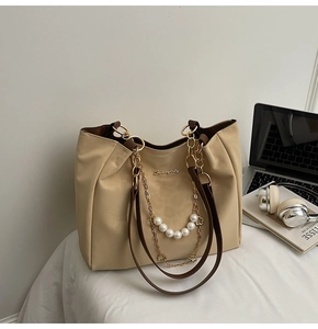 Detail of beige tote bag with pearl chain decoration and Sunnycity logo on a white surface