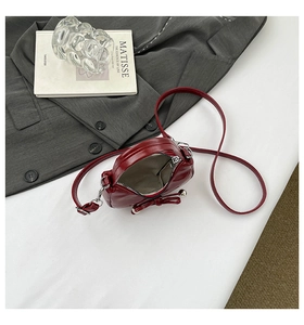 Détail d'un sac en cuir brillant bordeaux avec nœud décoratif et perles argentées