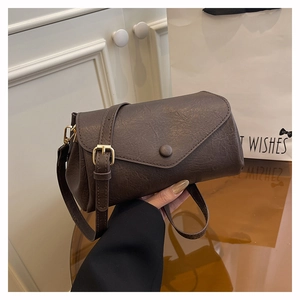 Detail of dark brown leather crossbody bag with flap and gold buckle on a wide strap
