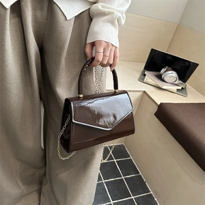 Dark brown patent leather handbag with gold chain strap shown in a 45-degree lifestyle view