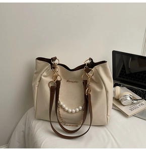 Close-up of pearl chain and gold metal link details on a white tote bag with laptop