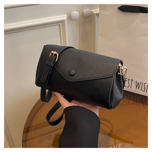 Detail of black vintage textured leather crossbody bag with gold snap and thin strap