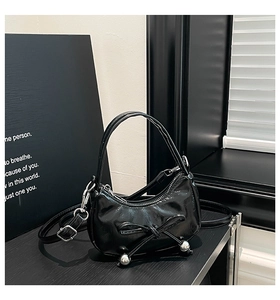 Détail du sac croissant en cuir verni noir avec nœud et breloques en métal argenté