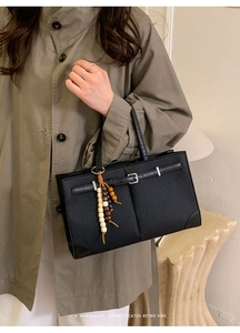 Detail of retro black tote bag with textured surface, metal buckle and beaded charm accessory