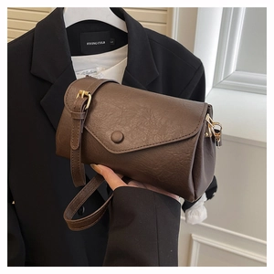 Close-up of a brown leather crossbody bag with a wide strap and decorative buckle