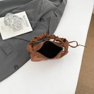 Brown suede handbag with scrunchie handle and silver zipper on a minimalist background