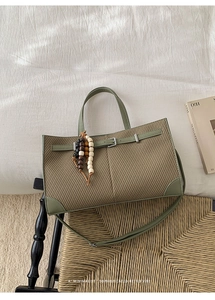 Detail of woven tote bag with green leather handles and beaded charm on a woven chair