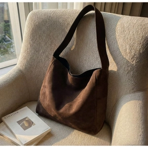 Détail de la texture d'un cabas en daim marron foncé posé sur un canapé beige chic