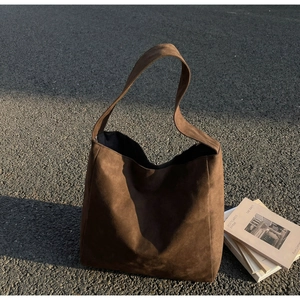 Détail du grand sac cabas en daim marron mat avec bandoulière large sur l'asphalte