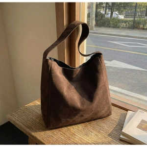 Grand sac cabas en daim marron posé sur un banc en bois vintage à côté d'une fenêtre