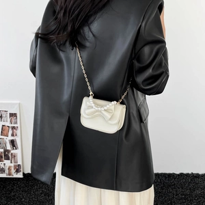 White pearl crossbody bag with leather bow and gold chain strap worn by a model