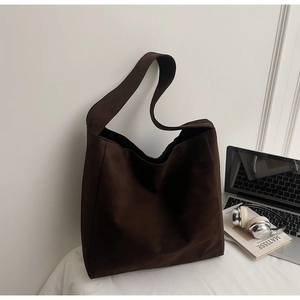 Detailed view of a dark brown suede hobo bag styled with a laptop and headphones