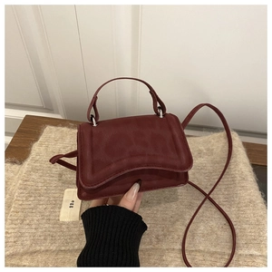 Detail of burgundy wavy flap handbag with leather strap and tiny egg fabric label