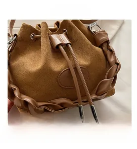 Dettaglio di borsa a secchiello in camoscio marrone con rifiniture in pelle intrecciata