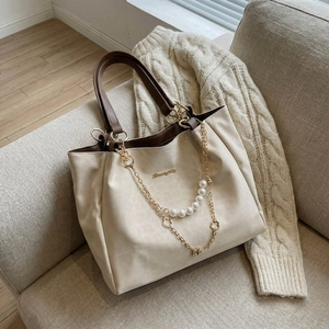 Minimalist cream leather tote bag with pearl chain detail on a cozy grey sofa