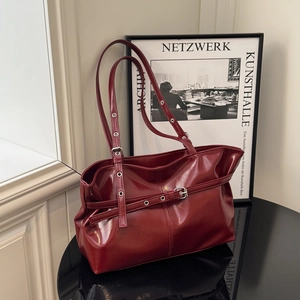 Deep red vintage faux leather tote bag with buckle details on a stylish table setup