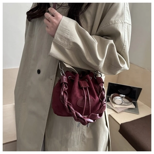 Detail of burgundy suede bucket bag featuring braided handle and drawstring closure