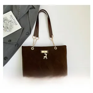 Detail of a brown suede tote bag with golden deer charm and chain shoulder strap