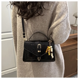 Detail of black faux crocodile leather bag with gold hardware and colorful bead pendant