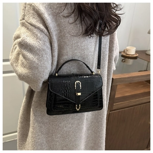 Detail of black stone-pattern handbag featuring golden horseshoe clasp on grey sweater