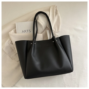 Detail view of black matte leather tote bag with silver studs on a stylish blazer
