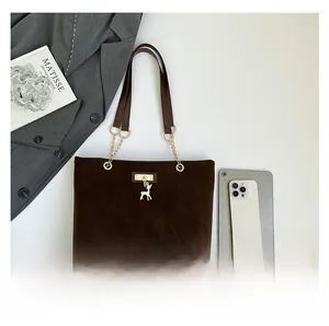 Detail of dark brown tote bag with matte texture, gold deer pendant and chain accents