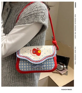Detail of checkered shoulder bag featuring red apple prints and a blue decorative bow