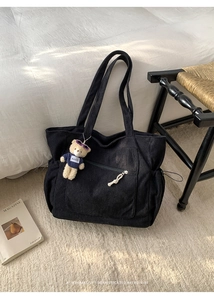 Detail of black corduroy tote bag featuring a front zipper pocket and cute bear pendant