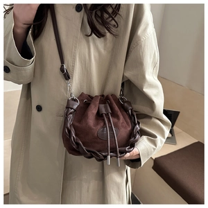 Dettaglio della borsa a secchiello in camoscio marrone con finiture in pelle intrecciata