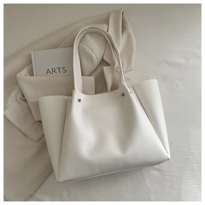 Detail of minimalist cream tote bag with metal rivets and slender straps for commute