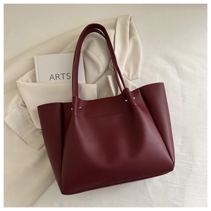 Close-up of deep wine red tote bag with slim straps and metal rivet details on texture