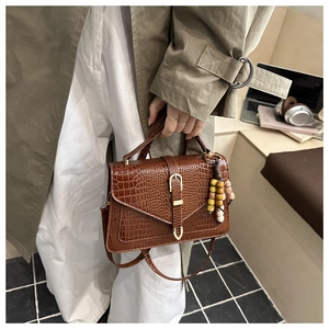 Close-up of brown crocodile embossed handbag with golden U-buckle and beaded tassel charm