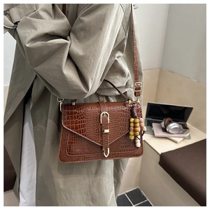 Close-up of brown crocodile texture leather bag with gold buckle and stylish bag charm