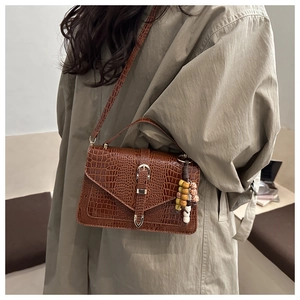 Borsa marrone con trama a coccodrillo e ciondolo a perline indossata con cappotto kaki
