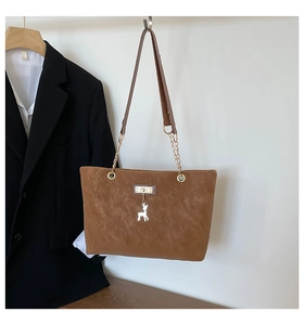 Detail of brown leather tote featuring gold chain straps and silver deer charm pendant