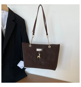 Detail of brown matte tote bag featuring gold deer charm and chain strap accents