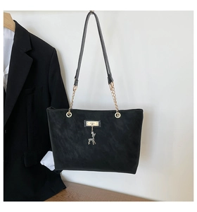 Close-up of black matte tote bag featuring gold deer pendant and elegant chain strap
