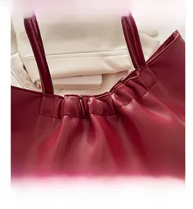 Detail view of the pleated closure and gold lettering on a red faux leather tote bag