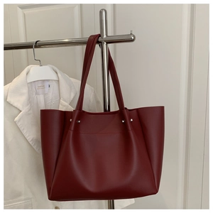 Detail view of a large burgundy tote bag in matte leather hanging on a rack