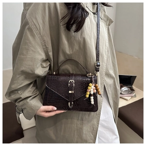 Detail of dark brown crocodile pattern handbag with colorful beads on khaki trench coat