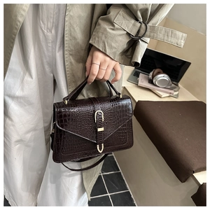 Detail of dark brown croc-effect handbag with gold U-buckle held by a model in a trench coat