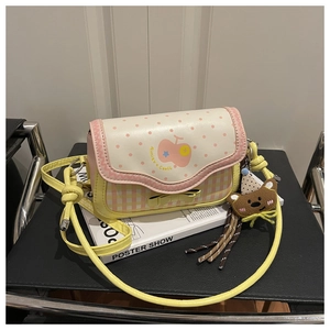 Close-up of pink checkered crossbody bag with apple print and bear charm on a chair