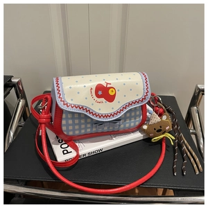 Detail of red apple print crossbody bag with cute teddy bear charm on book background