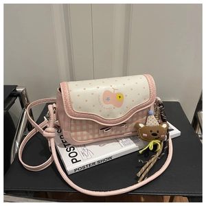 Detail of pink plaid crossbody bag with cartoon Bear pendant and polka dot flap design