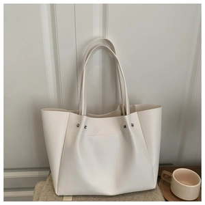 Detail of cream white tote bag featuring silver studs and soft pleated matte leather