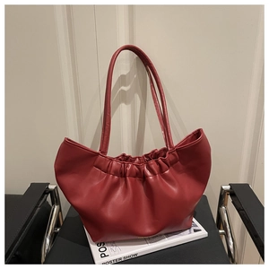 Close-up of red pleated cloud tote bag with slim handles resting on a black leather chair