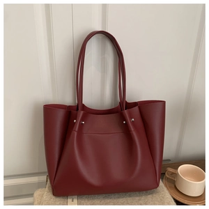 Detailed close-up of dark red tote bag with slim shoulder straps on white wood background