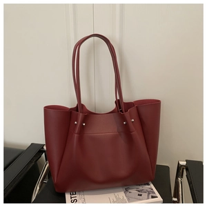 Deep burgundy leather tote bag with silver rivets and long handles on a black chair