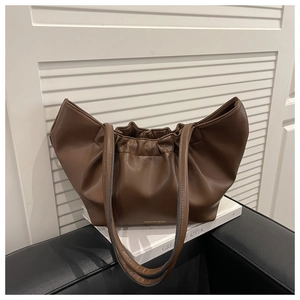 Detail of dark brown leather cloud bag with soft pleats on a white book surface