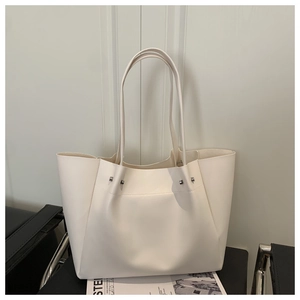Detail shot of white matte leather tote bag featuring silver studs and slim shoulder straps